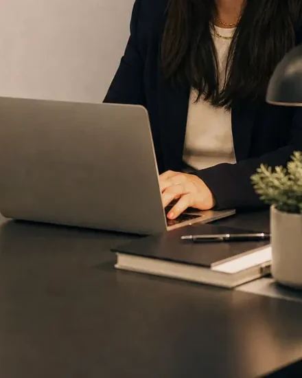Mesa de trabalho à noite, com notebook aberto e a cidade acesa ao fundo